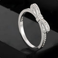 A silver couple-style ring with a bow shape decorated with rhinestones and zircon crystals.