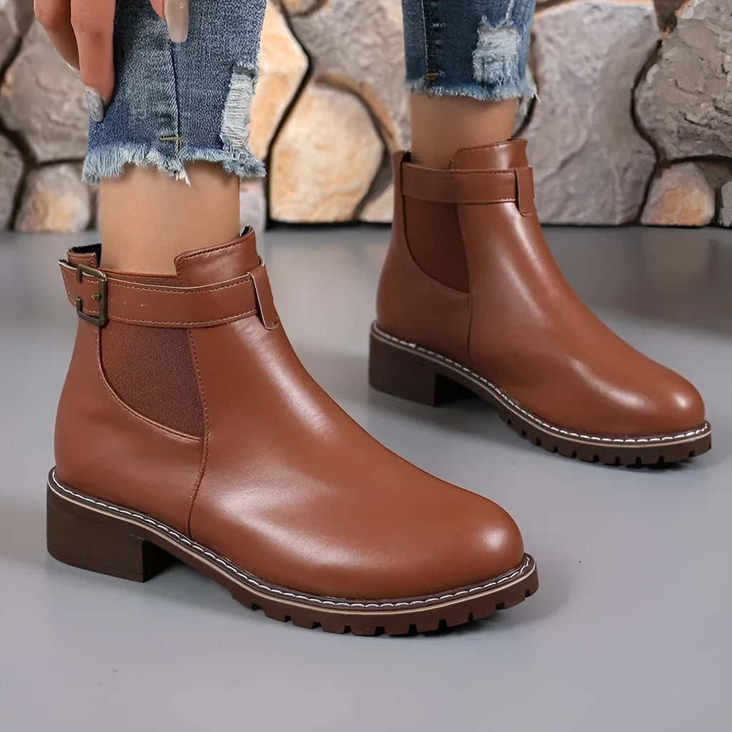Black round toe ankle boot with a silver belt buckle decoration on the side.