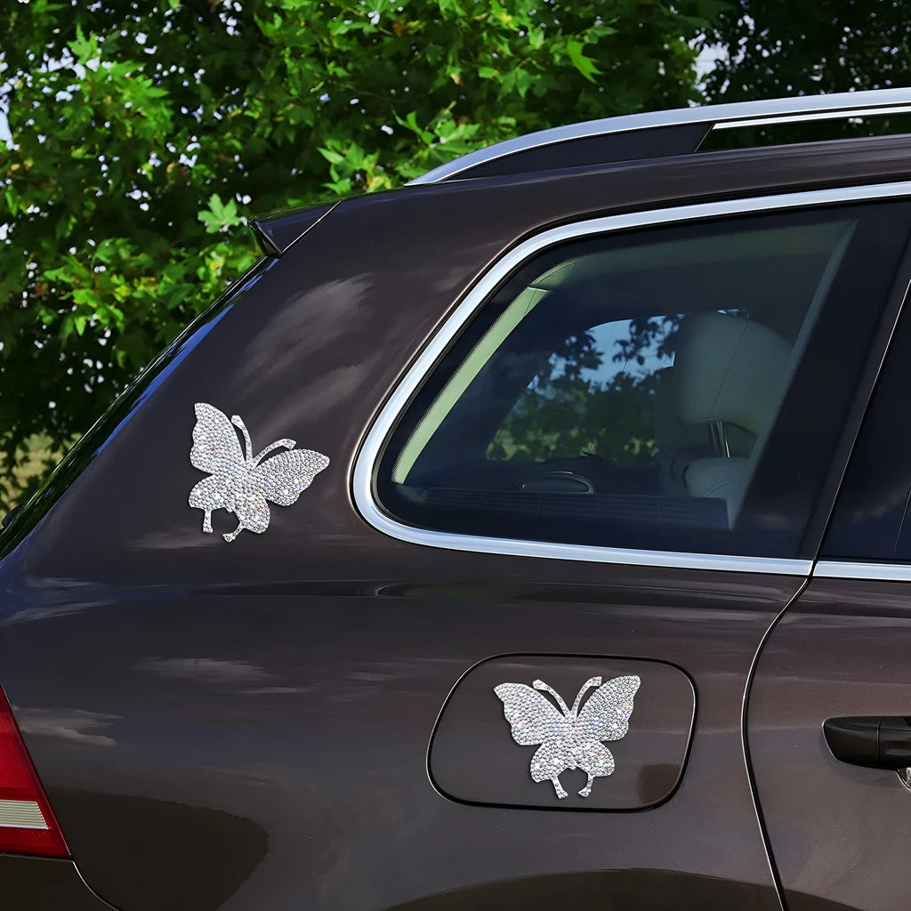 Close-up of a diamond-encrusted glass car sticker in butterfly and bear paw designs on a clear background.