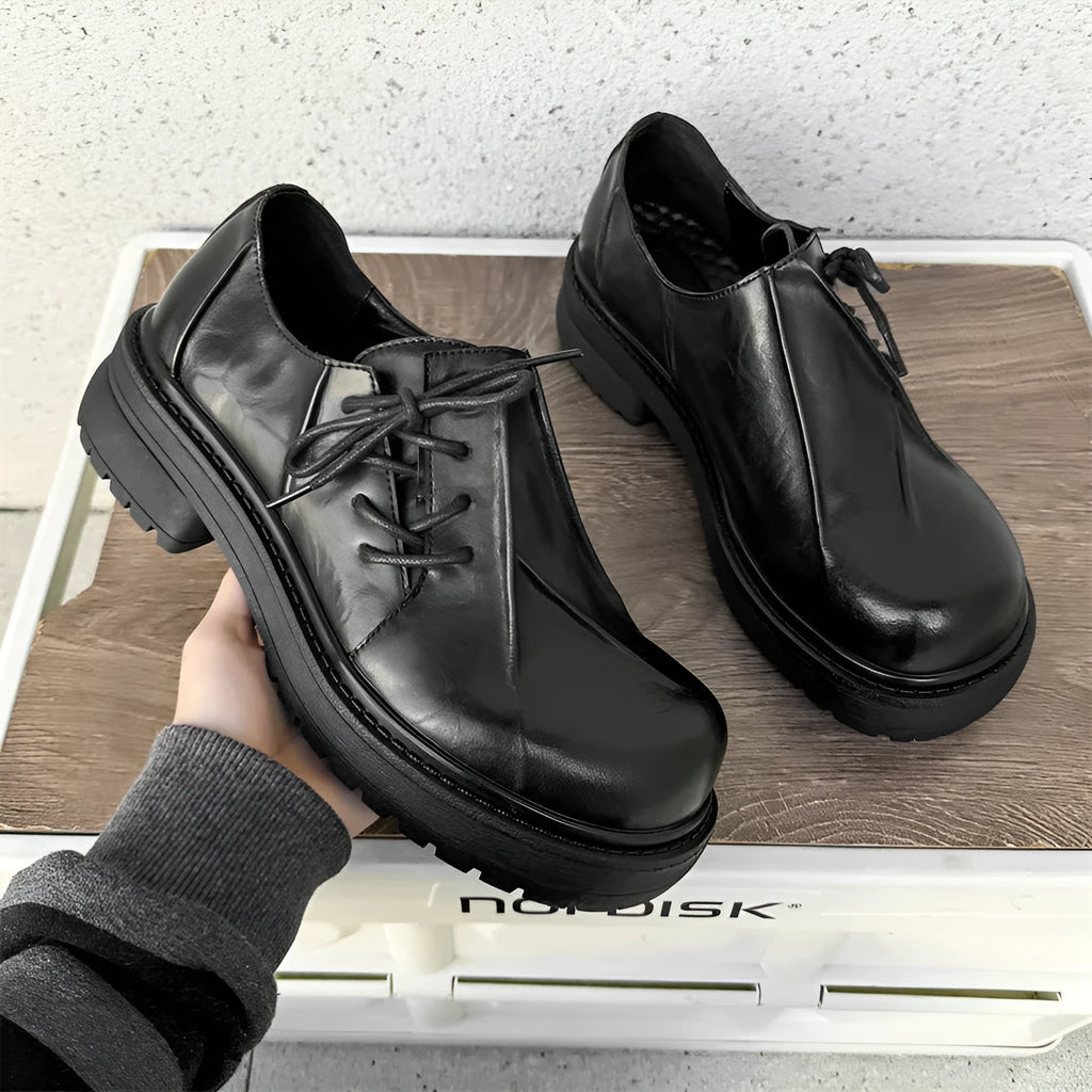 Black leather platform shoes with a warped head design and round toe on a rubber sole.