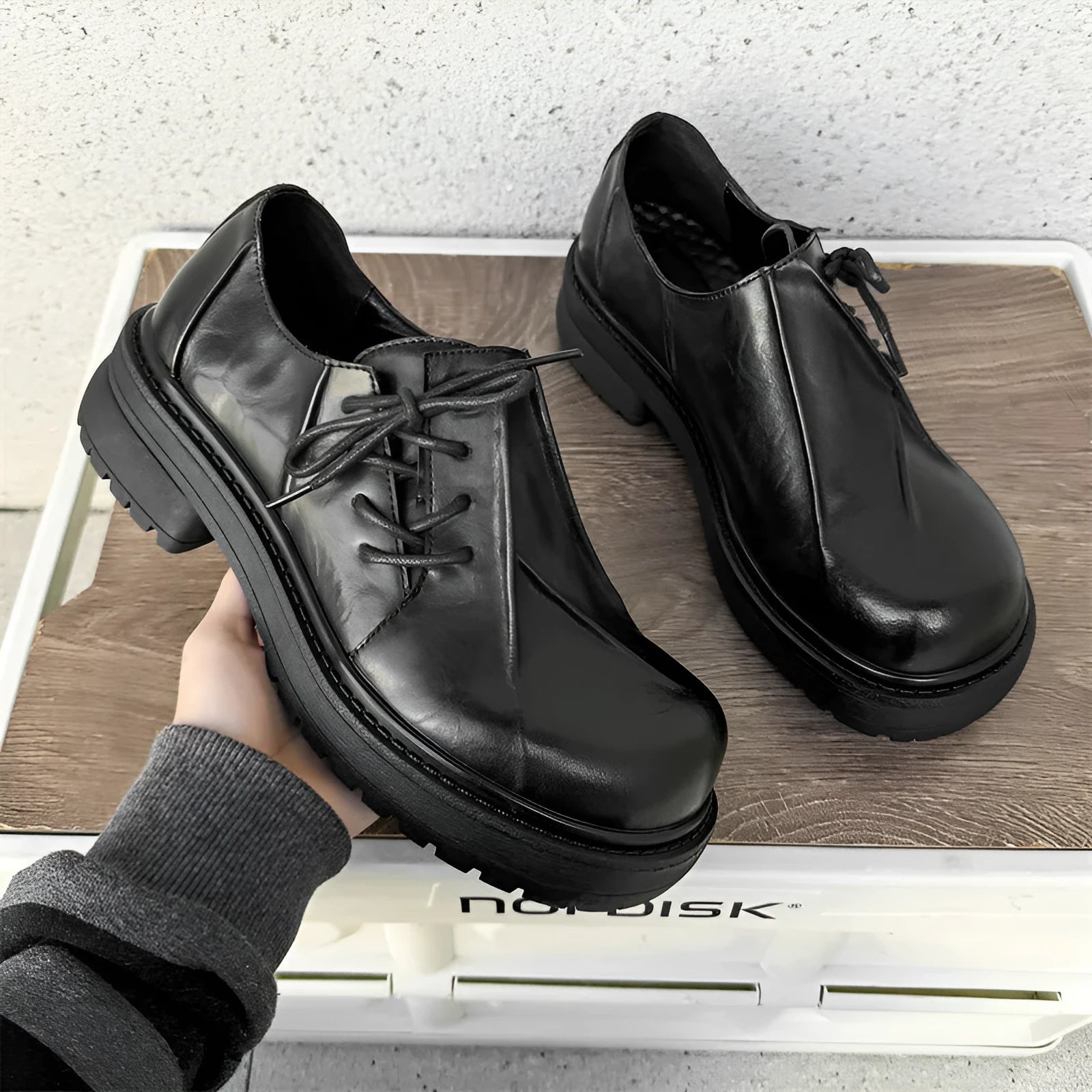 Black leather platform shoes with a warped head design and round toe on a rubber sole.