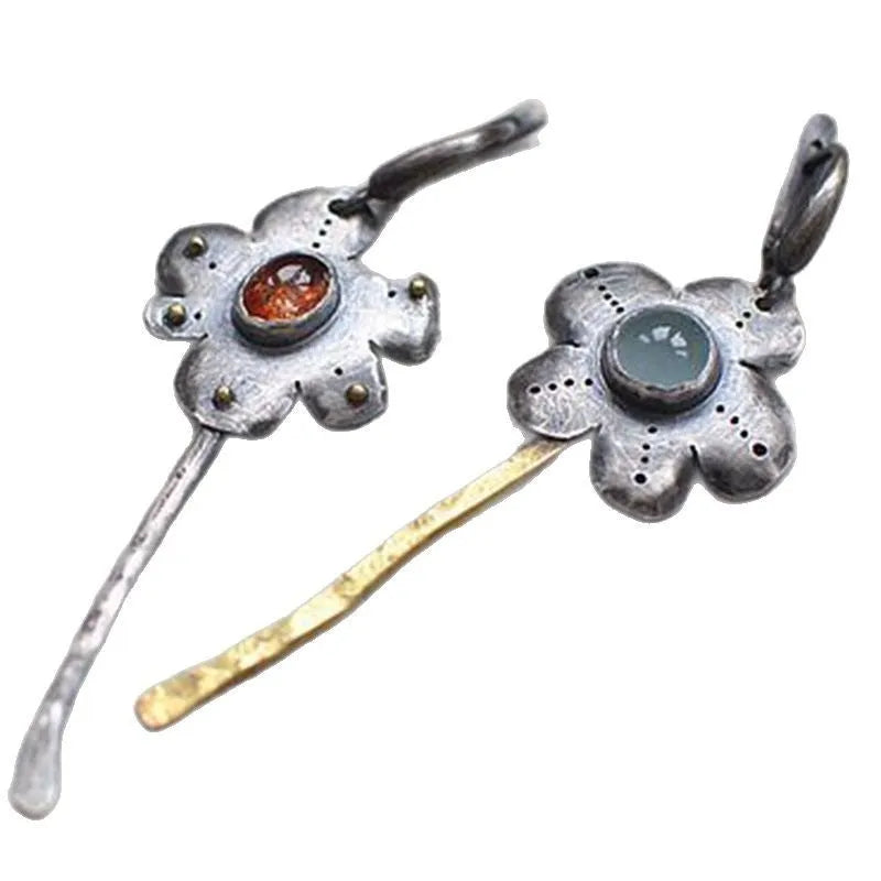 A pair of long, geometric flower-shaped retro earrings in two contrasting metallic colours with an asymmetrical design.