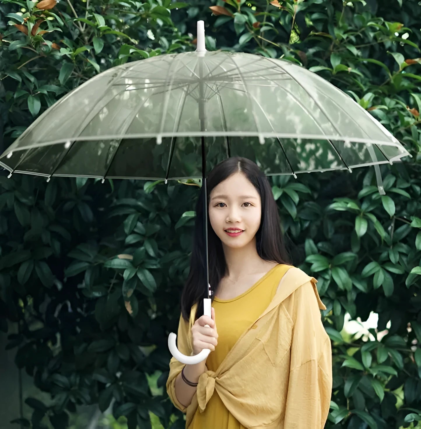 Long-handled transparent umbrella with black steel frame and white handle on a black background.