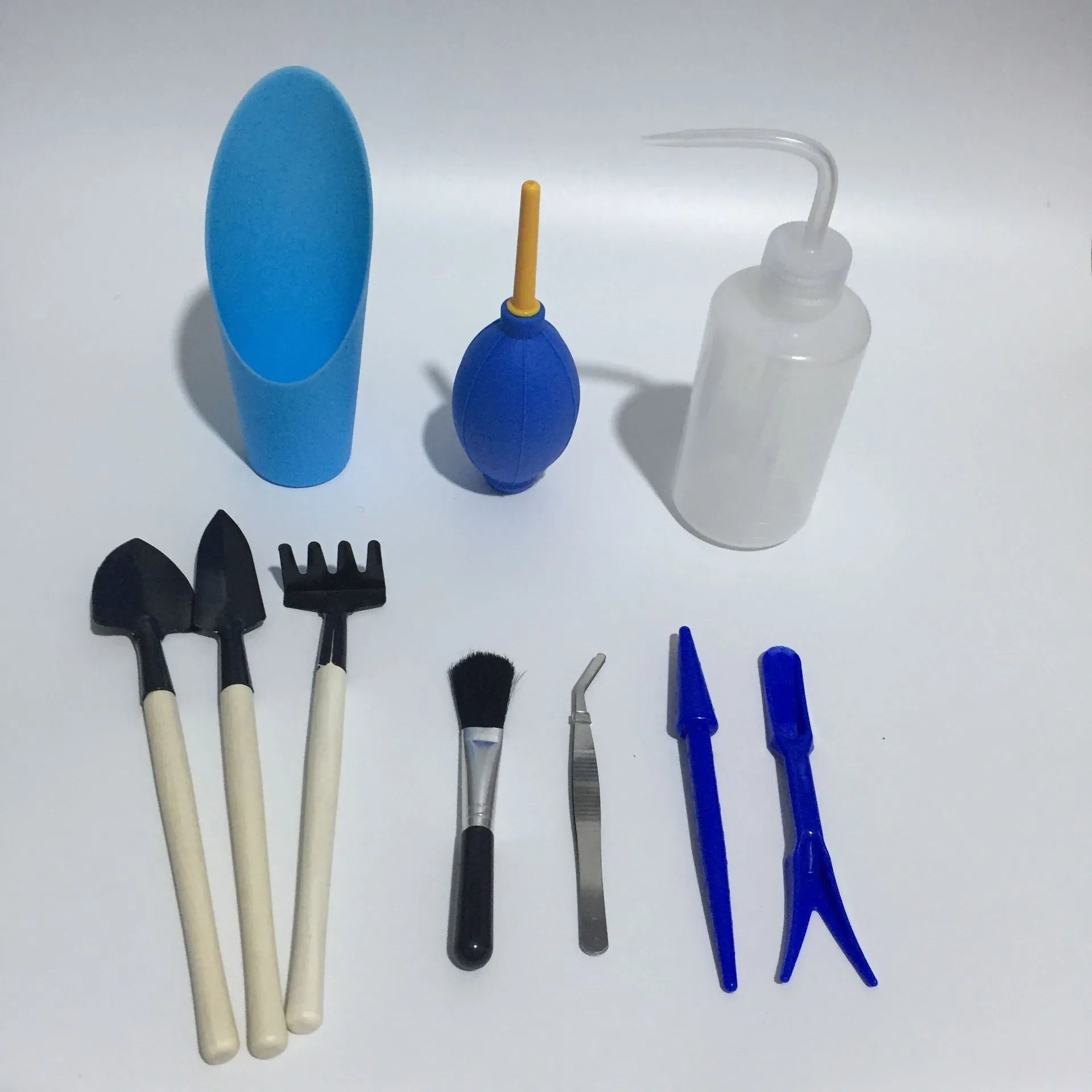 Succulent gardening tool set showing drip kettle, tweezers, mini shovel, rake, and other small plant care tools on a table.