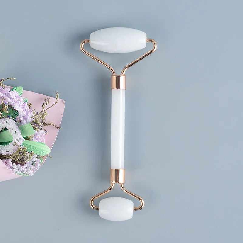 White jade double-headed facial roller and scraping board set on a flat surface.