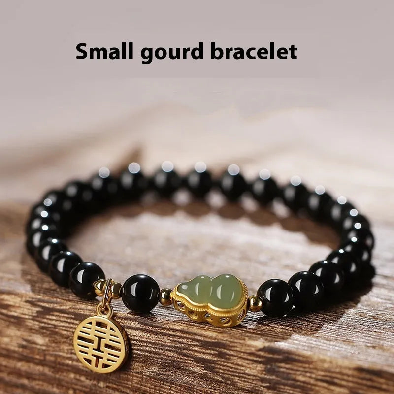 Black obsidian bracelet with a green Hetian jade gourd charm on a wrist.