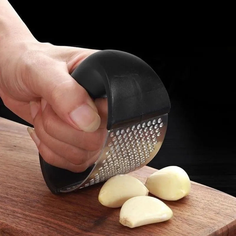 Stainless steel garlic press with ergonomic black handle on a kitchen counter.