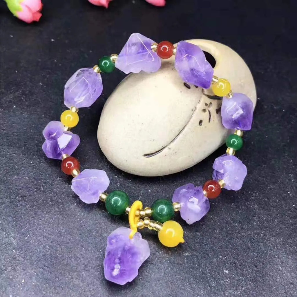 Close-up of a women's bracelet with natural shaped amethyst beads and a silver fu charm on a white background.
