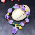 Close-up of a women's bracelet with natural shaped amethyst beads and a silver fu charm on a white background.