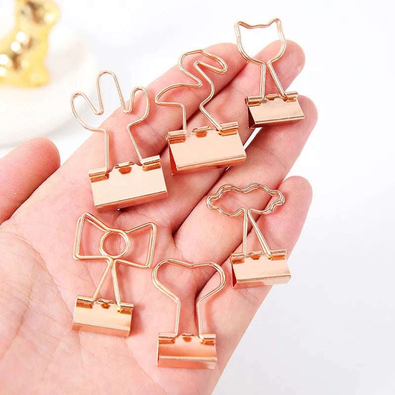 Small gold metal office clip with a decorative bow charm on a long tail.