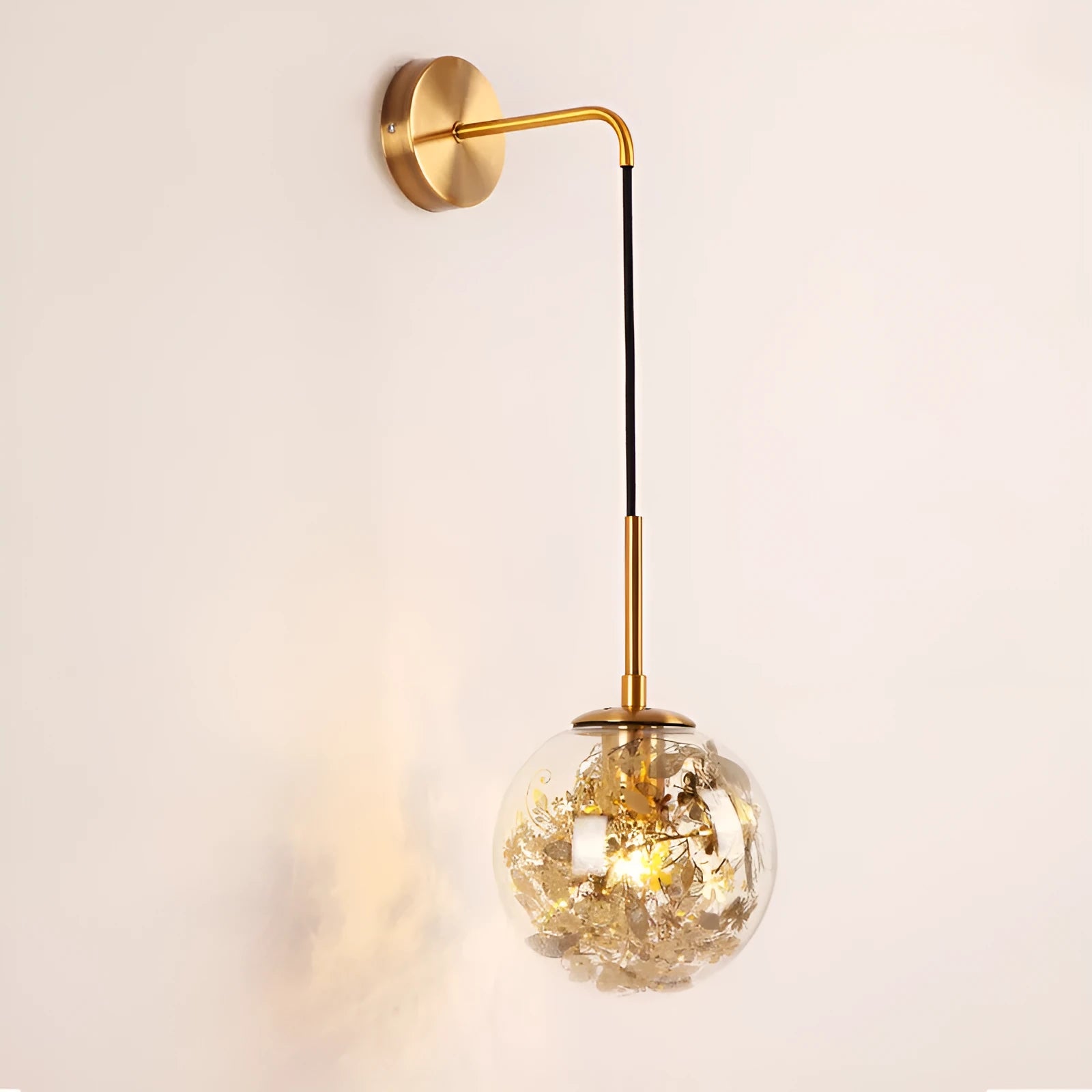 Modern round glass wall lamp in golden flower finish mounted beside a bed.