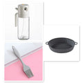 Glass oil sprayer bottle with grey cap, shown in spray and pour modes next to cooking ingredients.