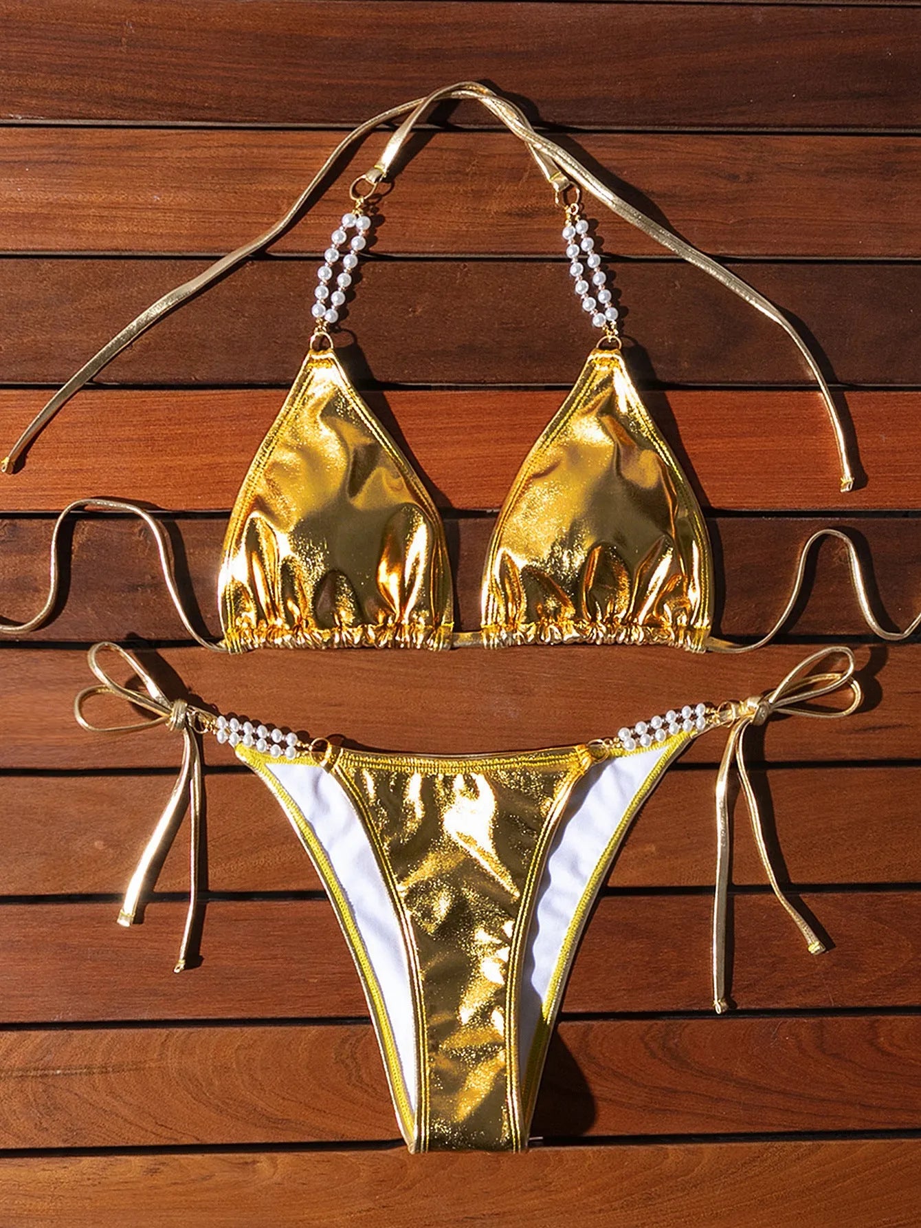 Gold bronzing effect women's halter neck bikini with lace-up back and pearl chain detail on mannequin