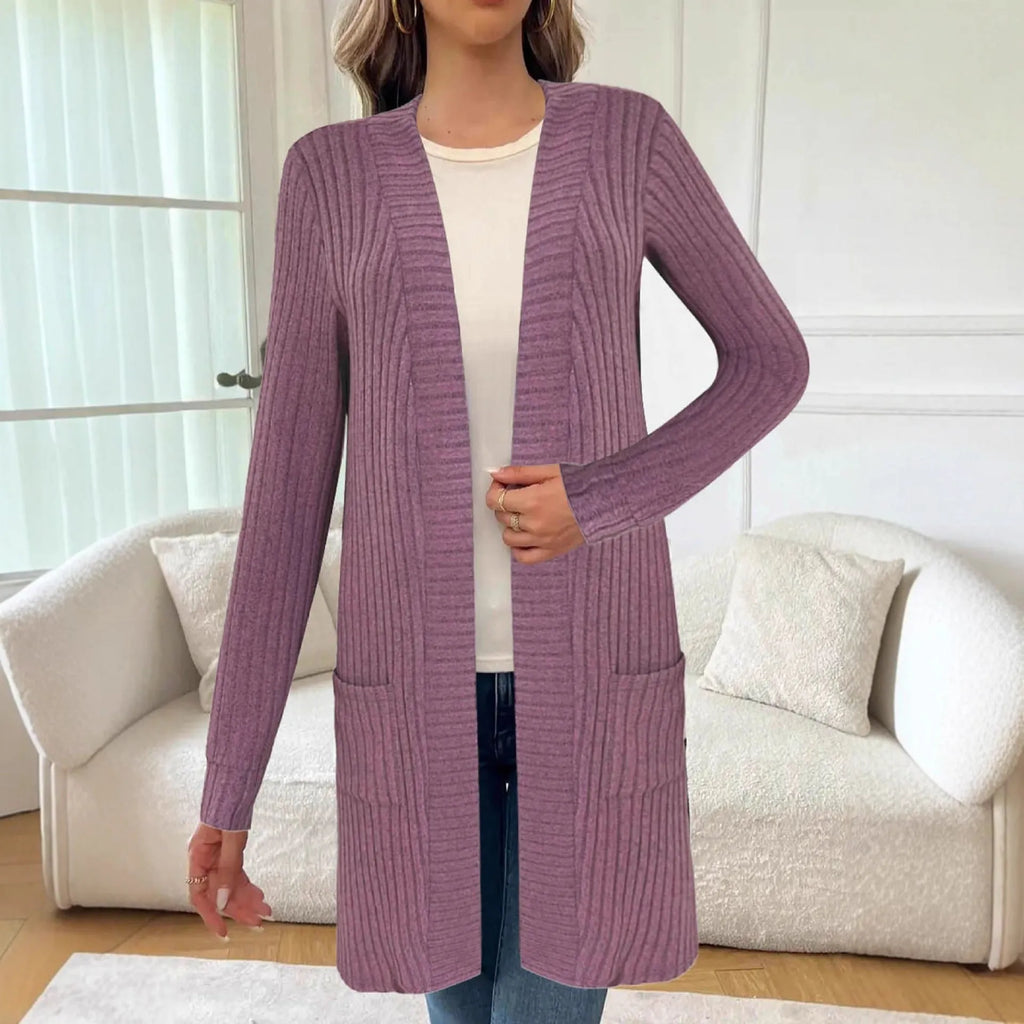 A woman wearing a loose grey knitted cardigan jacket with long sleeves and patch pockets.