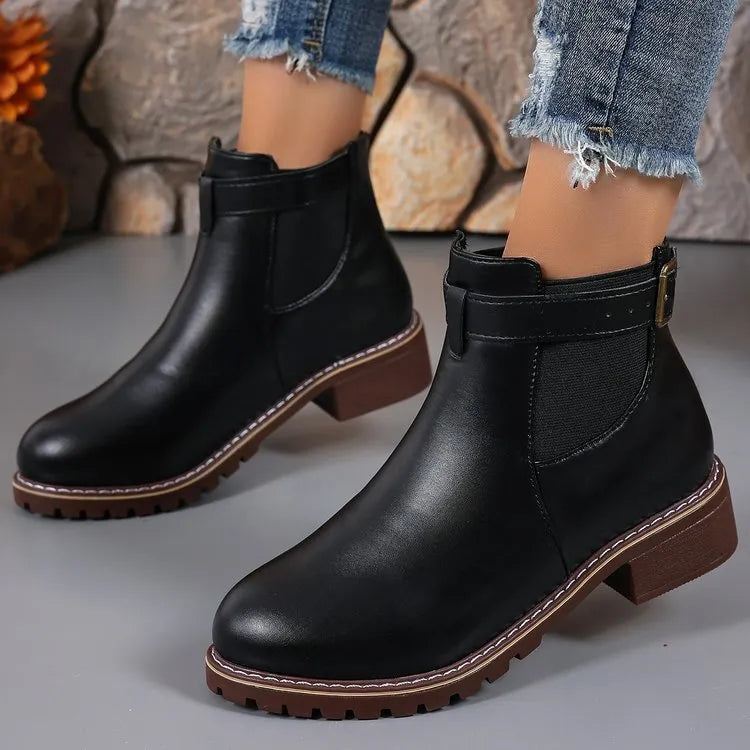 Black round toe ankle boot with a silver belt buckle decoration on the side.