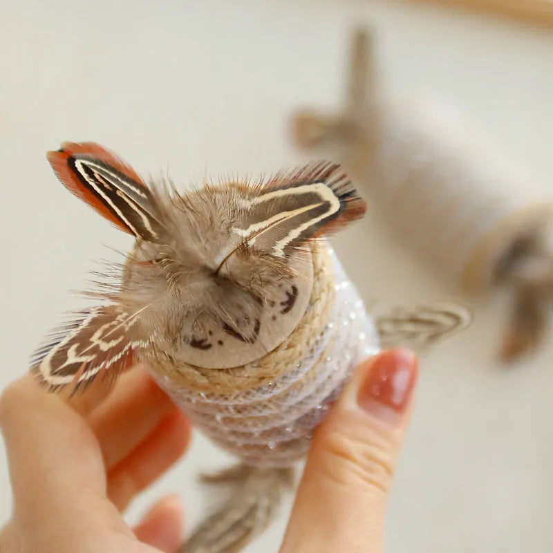 Beige cat toy with hemp rope scratching area, sound-making roller ball, and feather attachments.