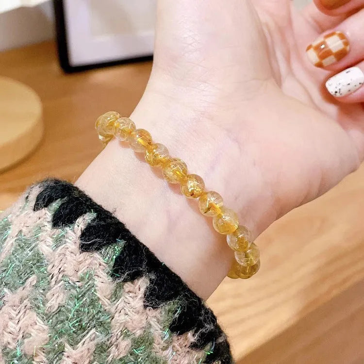 Gold rutilated quartz sunstone bracelet with diamond shapes and round beads on female wrist