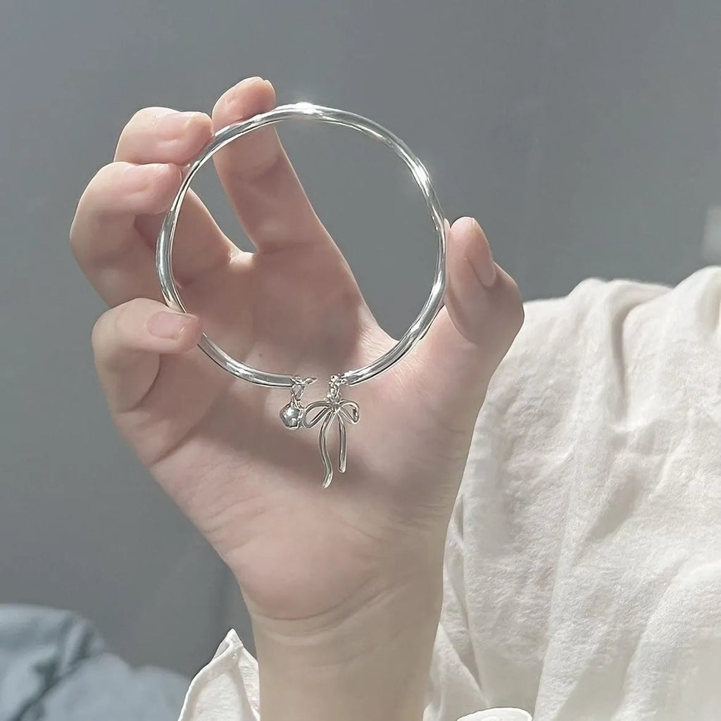 Close-up of a silver-toned adjustable bracelet with a bow bell charm on a model's wrist.