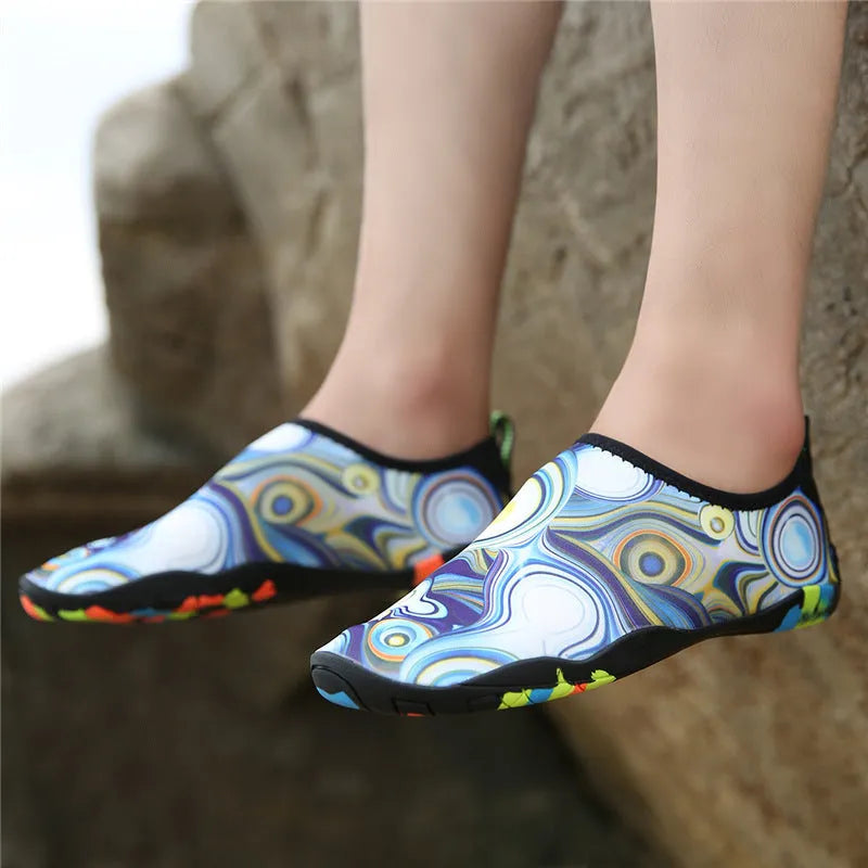 Blue Lycra beach wading shoes with decorative printing, shown on a sandy background