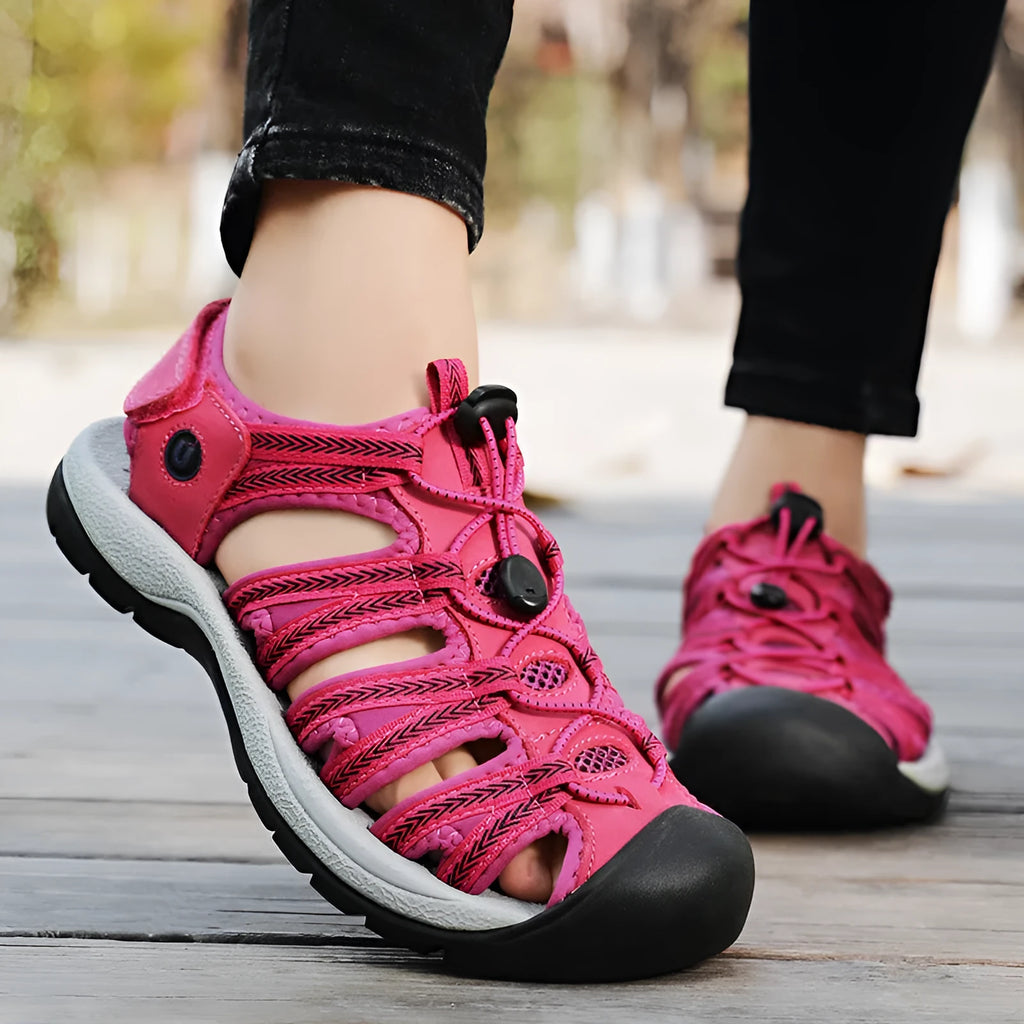 Women's black leather mesh toe box sandals with elastic band and rubber sole on a beach