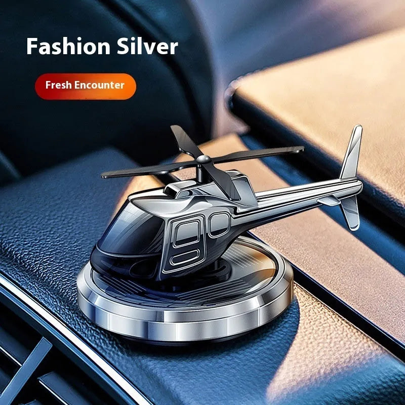 Silver metal solar-powered rotating helicopter car air freshener ornament on a dashboard.