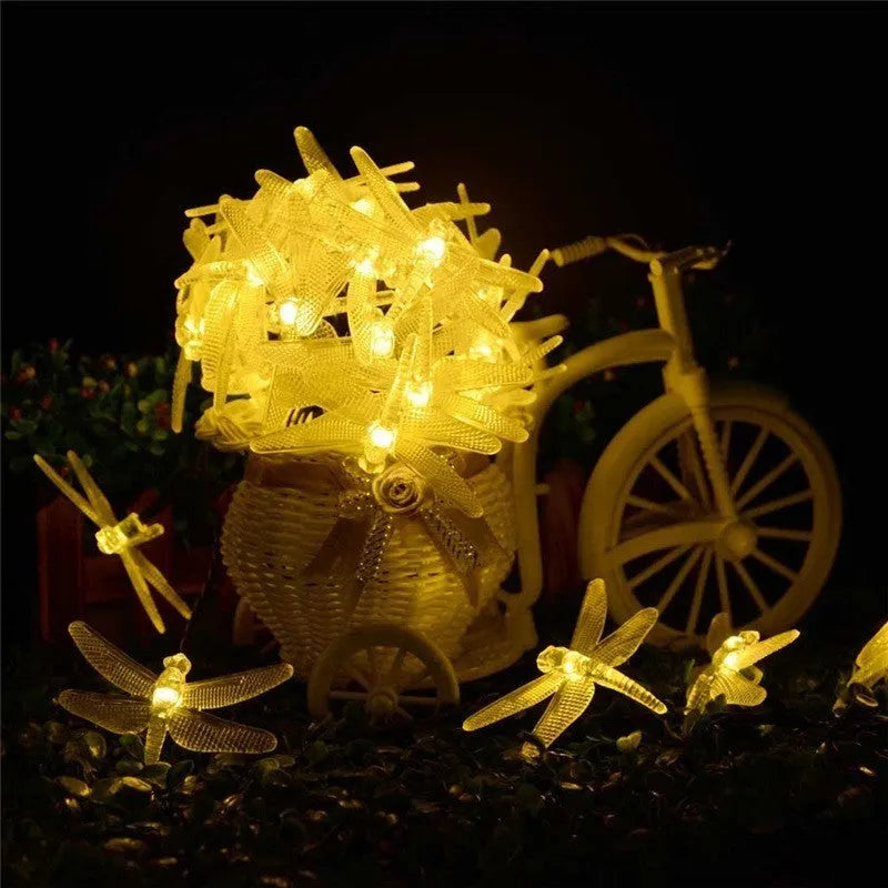 Outdoor solar-powered dragonfly string lights with garden spike, shown in a warm white glow