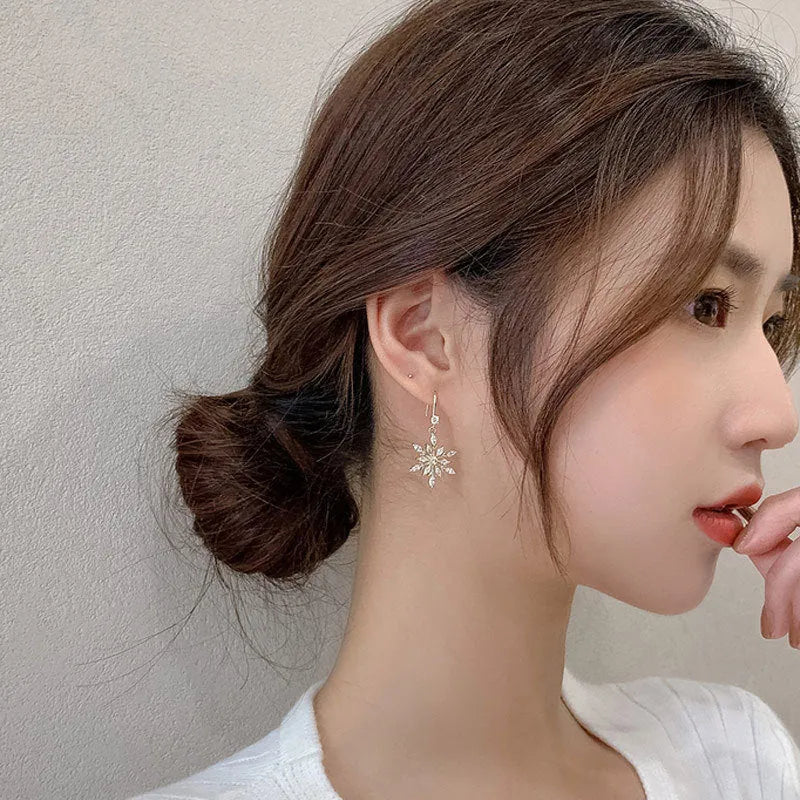 Gold alloy snowflake drop earrings with clear zircon centre on a white background