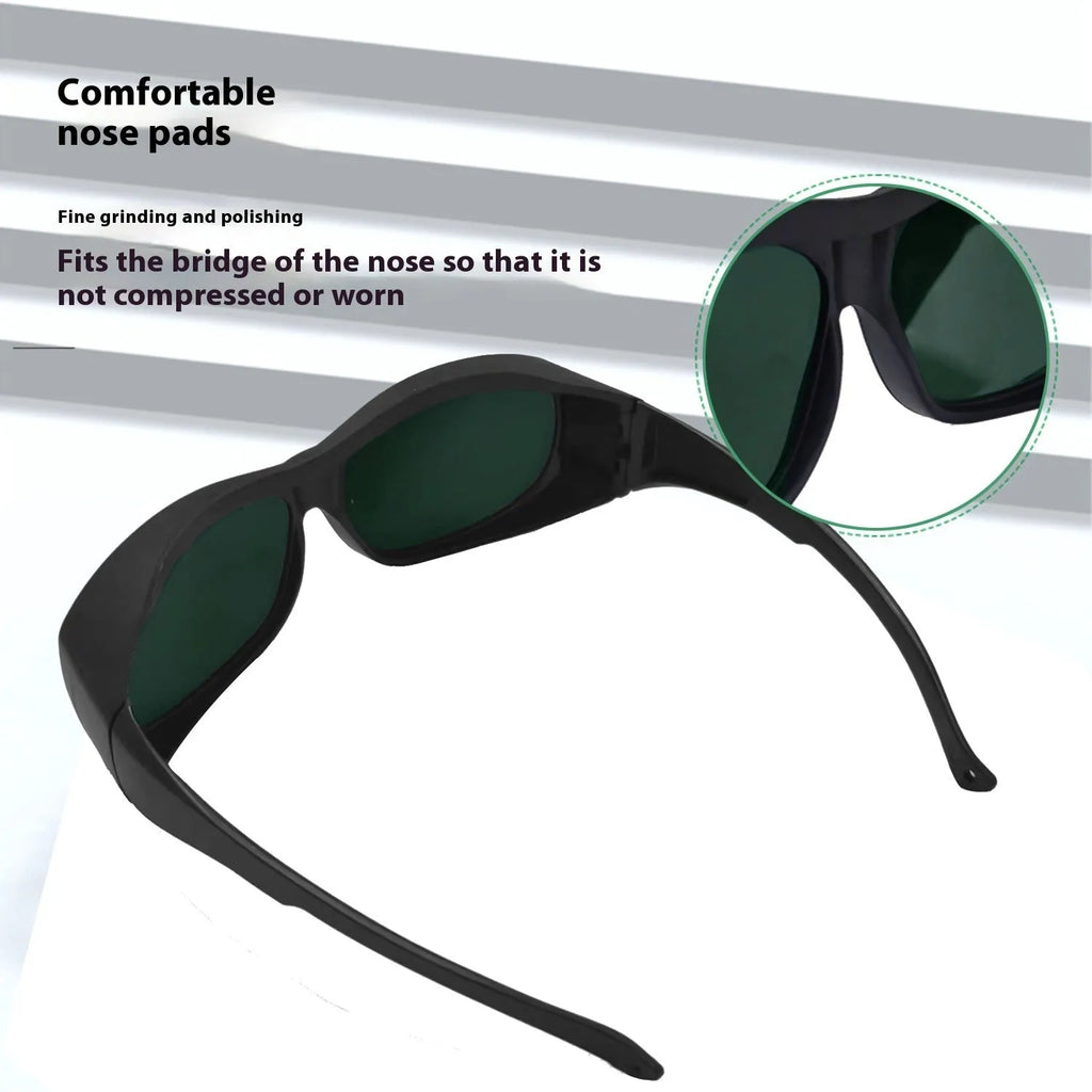 A pair of clear laser and welding safety goggles with a soft cleaning cloth on a dark background.