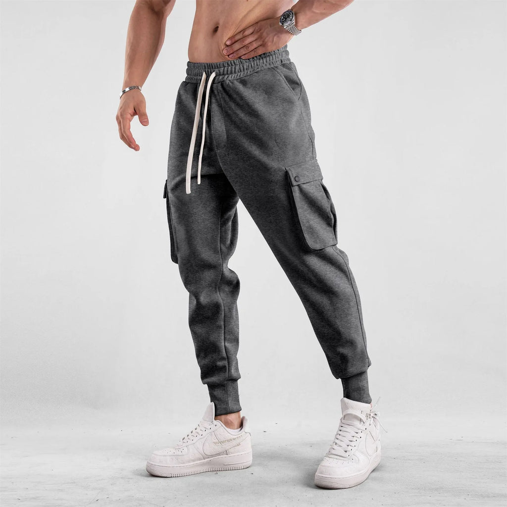 Man wearing loose light grey cotton sports trousers with ankle ties and multiple pockets.