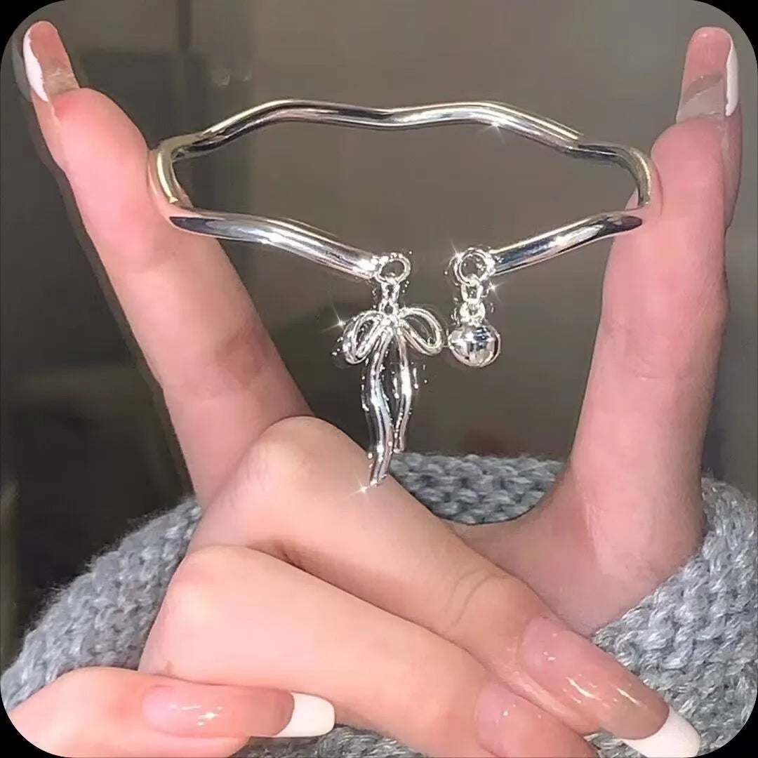 Close-up of a silver-toned adjustable bracelet with a bow bell charm on a model's wrist.