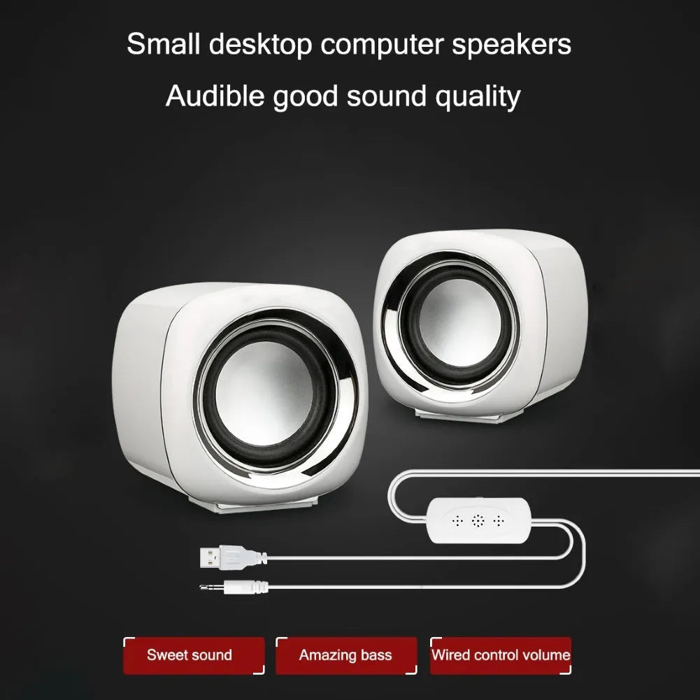 Pair of compact black wired desktop computer speakers with 3.5mm plug next to a laptop.