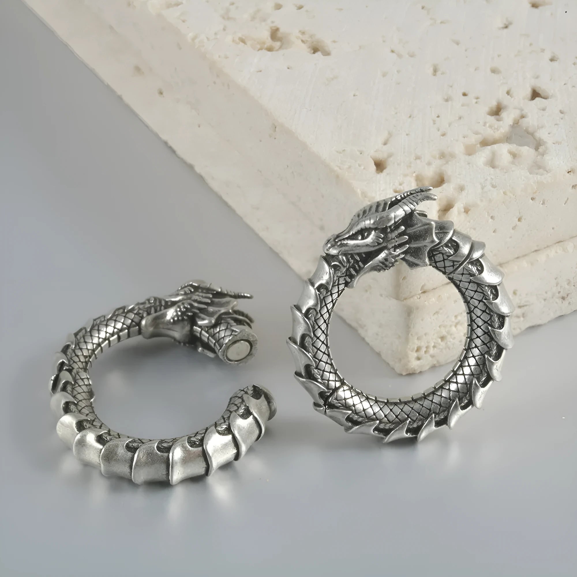 A pair of large antique silver hoop earrings with a hollow-out geometric dragon shape design.