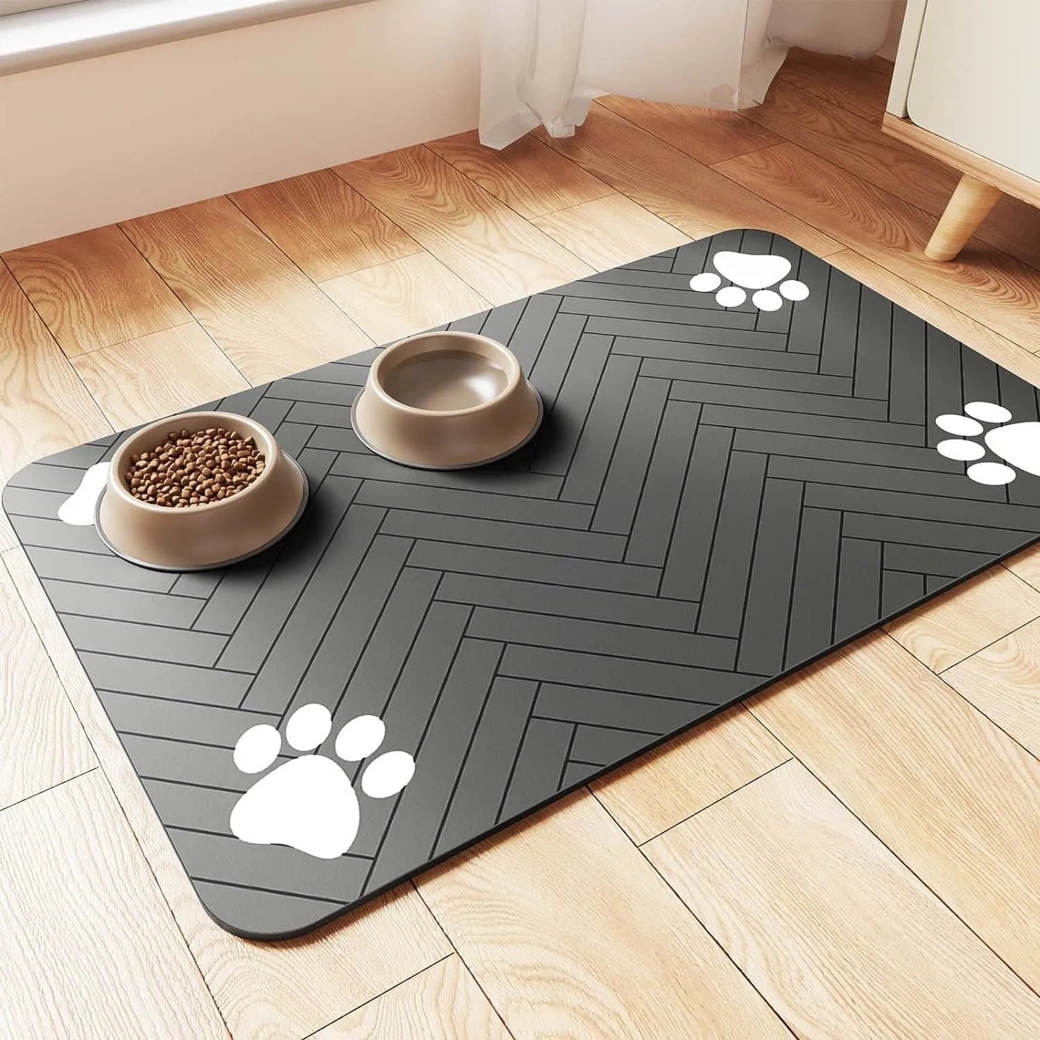 A rectangular diatom ooze pet feeding mat in grey placed under a dog's water and food bowls on a kitchen floor.