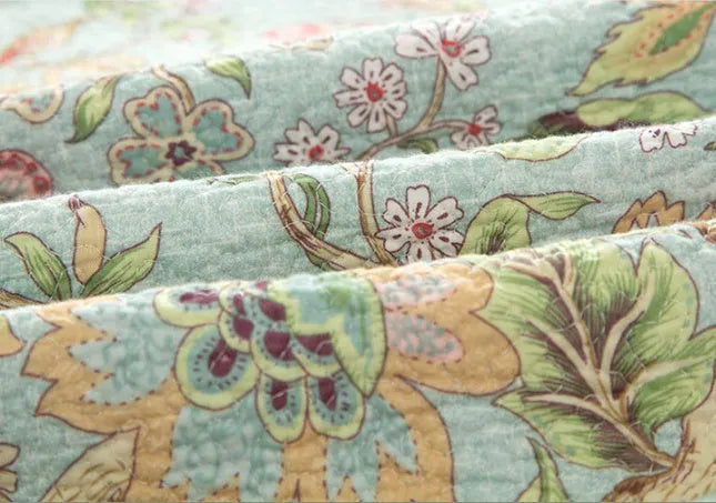 Blue American floral and bird pattern quilted cotton bedspread laid flat on a bed.