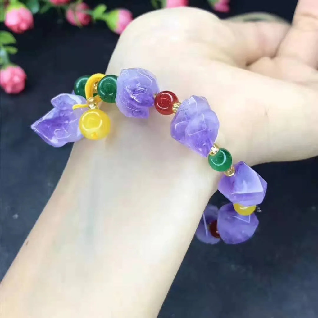 Close-up of a women's bracelet with natural shaped amethyst beads and a silver fu charm on a white background.