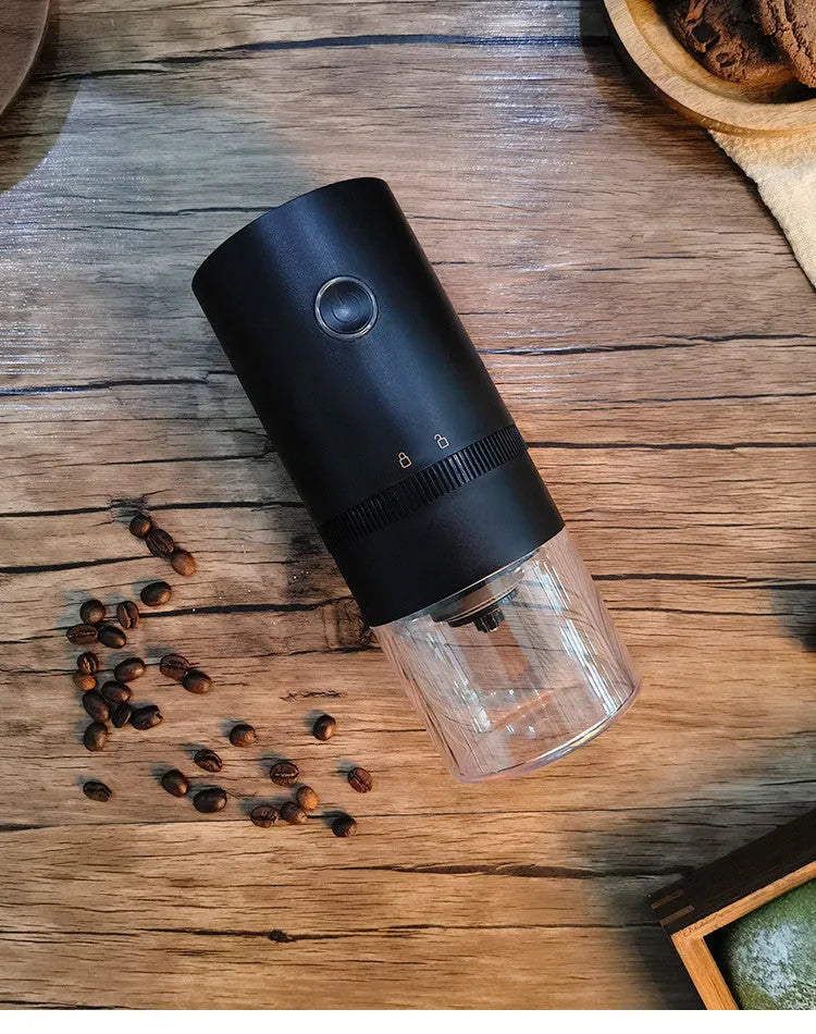 Black portable electric coffee grinder with transparent chamber showing coffee beans, USB-C charging port visible