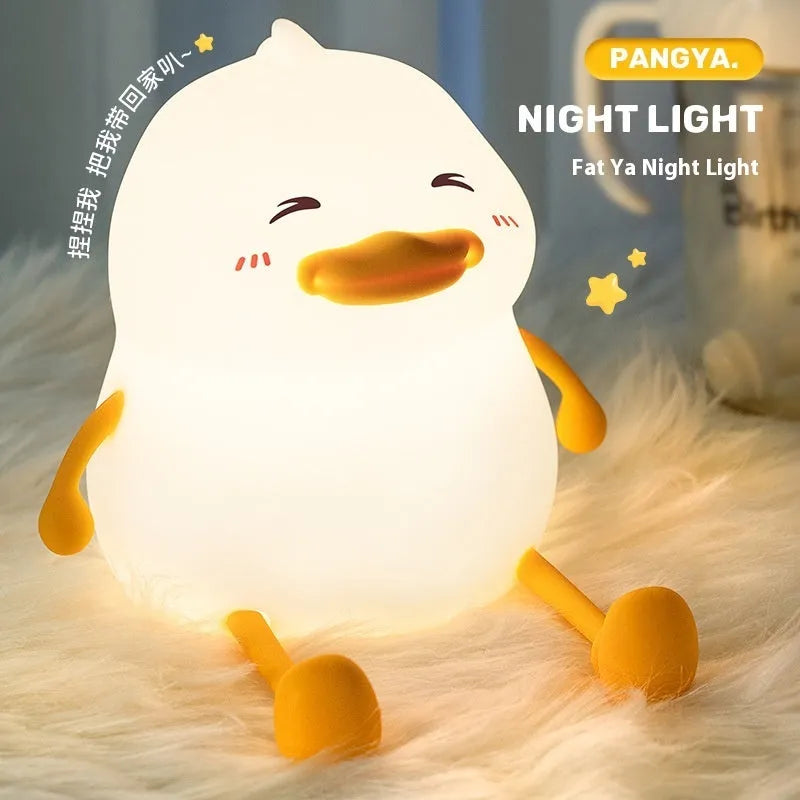 Chubby silicone pat night light on desk holding a mobile phone, showing soft glow.
