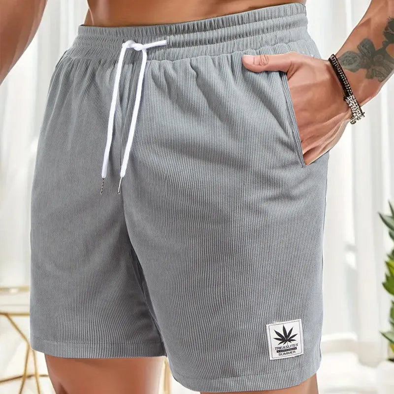 Man wearing grey straight-cut elastic drawstring summer shorts on a beach.