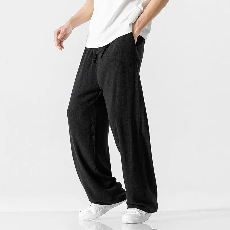 Man wearing beige straight-leg cropped linen-style trousers with a drawstring waist.