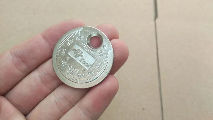 Round zinc alloy spark plug gauge with dual scales on a white background
