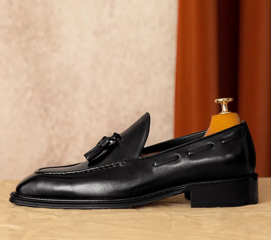 Men's black genuine leather loafers with fringe detail and a rubber sole, shown from a side angle.