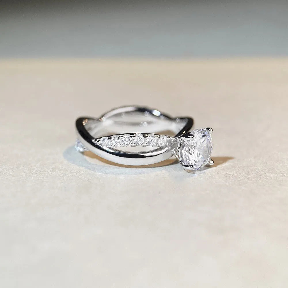 A silver moissanite ring with a 1 carat stone in a four-claw setting and a twisted geometric band.
