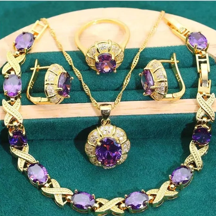 Gold plated necklace, earrings, ring, and bracelet set with blue cubic zirconia stones on a grey background.