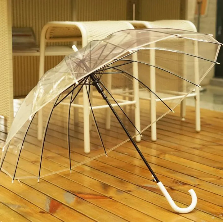Long-handled transparent umbrella with black steel frame and white handle on a black background.