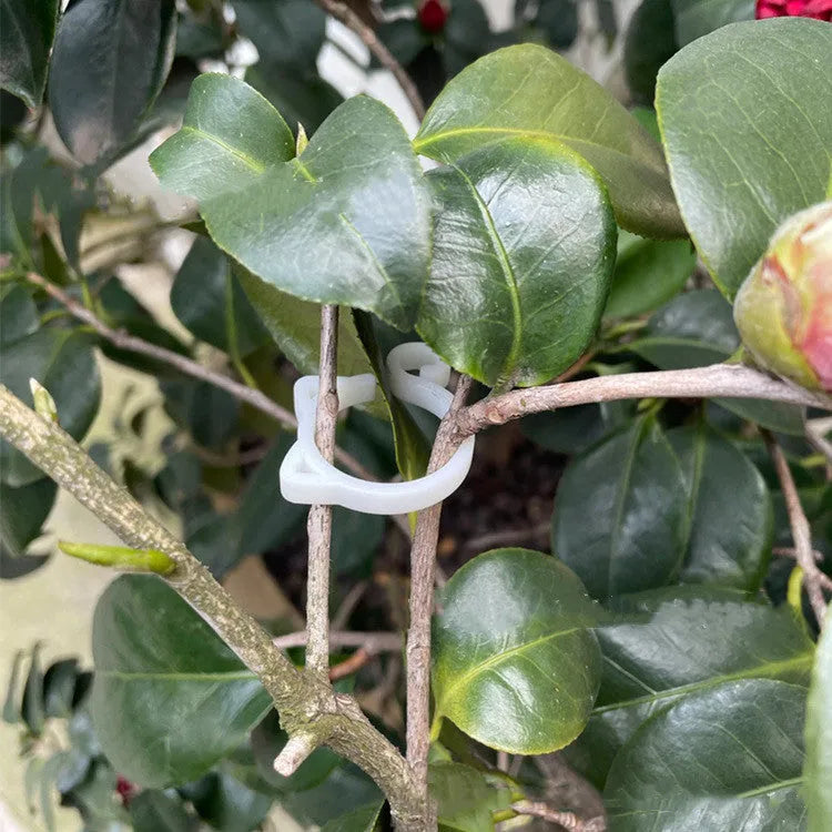 A red cat-shaped plastic clip for holding plant stems against a support stake.