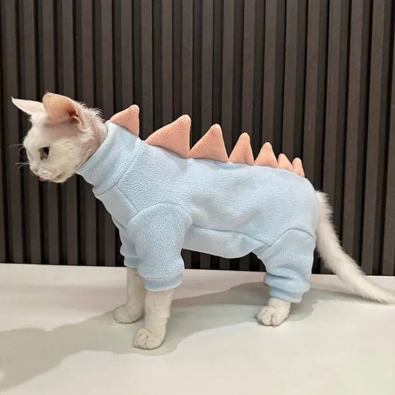 Sphynx cat wearing a green fleece dinosaur costume with a tail and back spikes