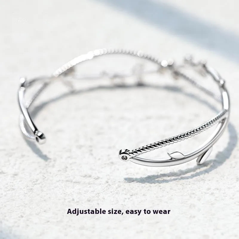Close-up of a white gold coloured twisted branch sprout design bracelet on a wrist.