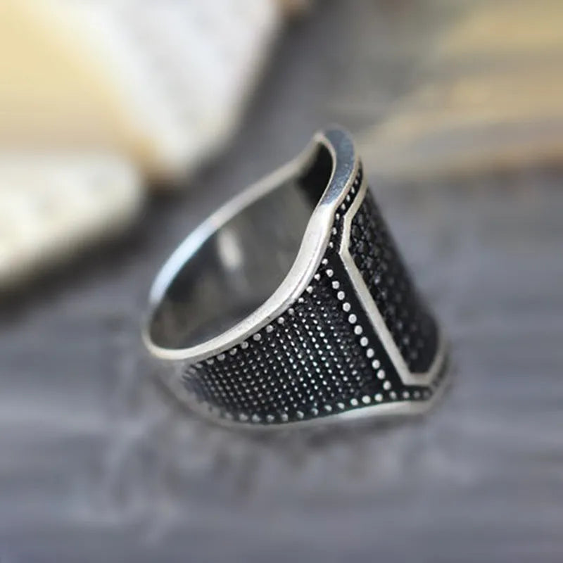 Black alloy ring with copper inlay and a central zircon stone, shown on a finger.