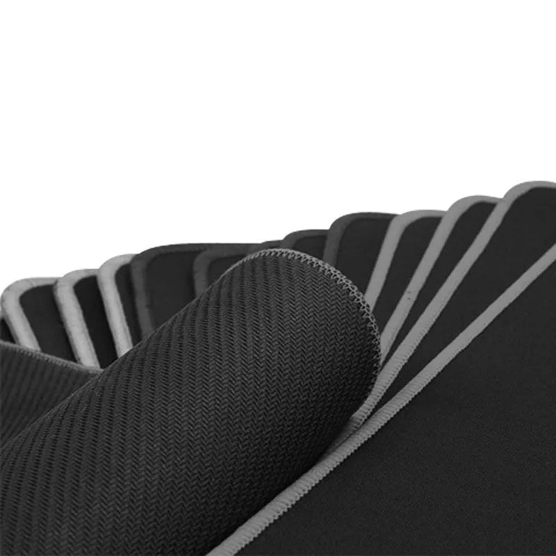 All black extra long desk mat with overlock stitching on a wooden desk with keyboard and mouse.