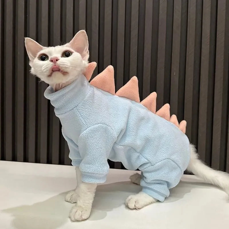Sphynx cat wearing a green fleece dinosaur costume with a tail and back spikes